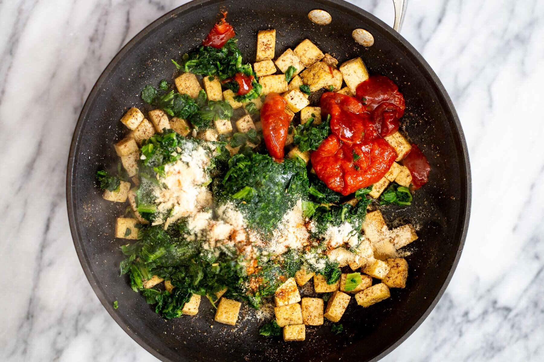 tofu cubes in a frying pan with red bell pepper and spinach