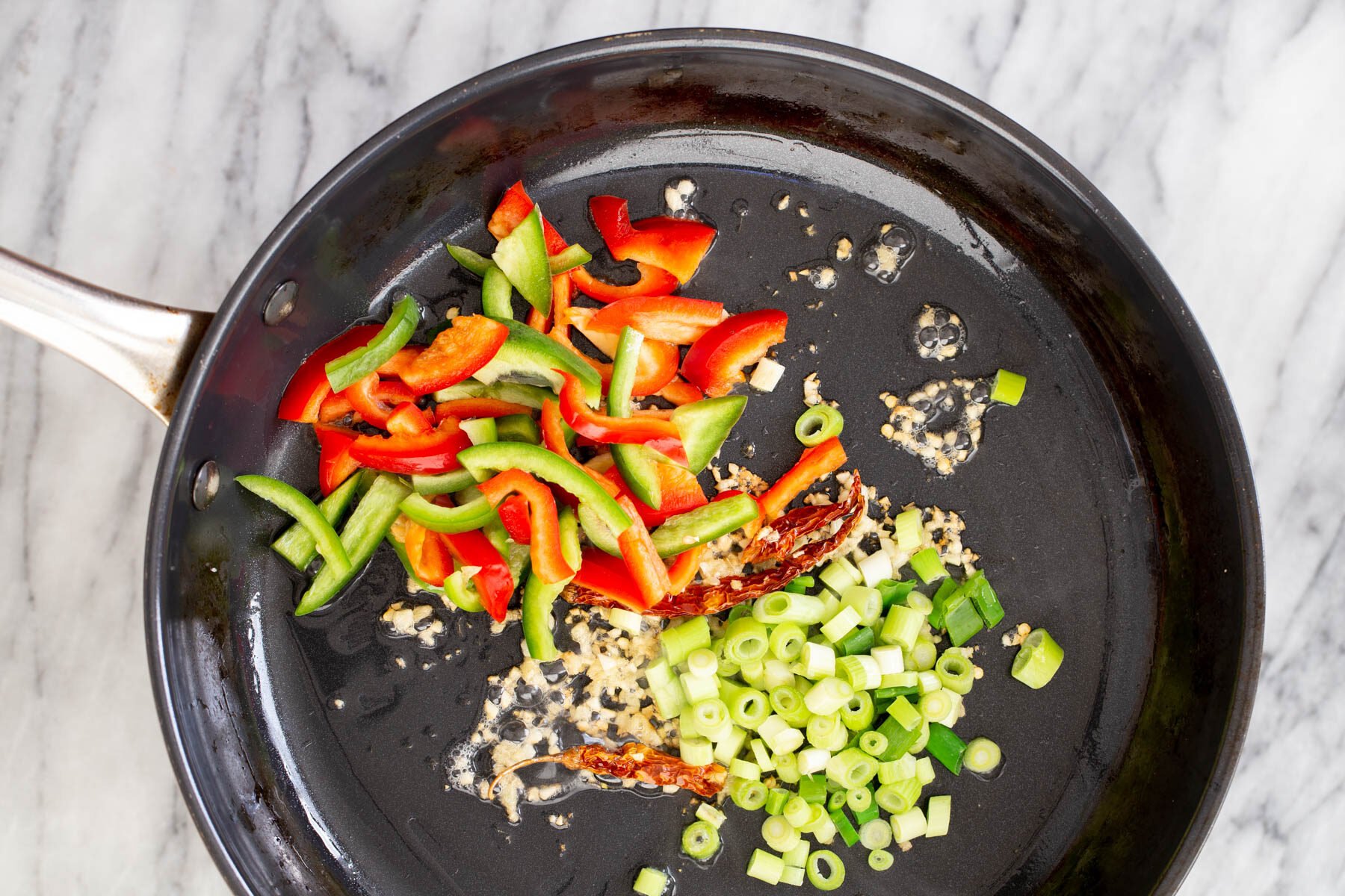 bell peppers spring onions and garlic in a frying pan