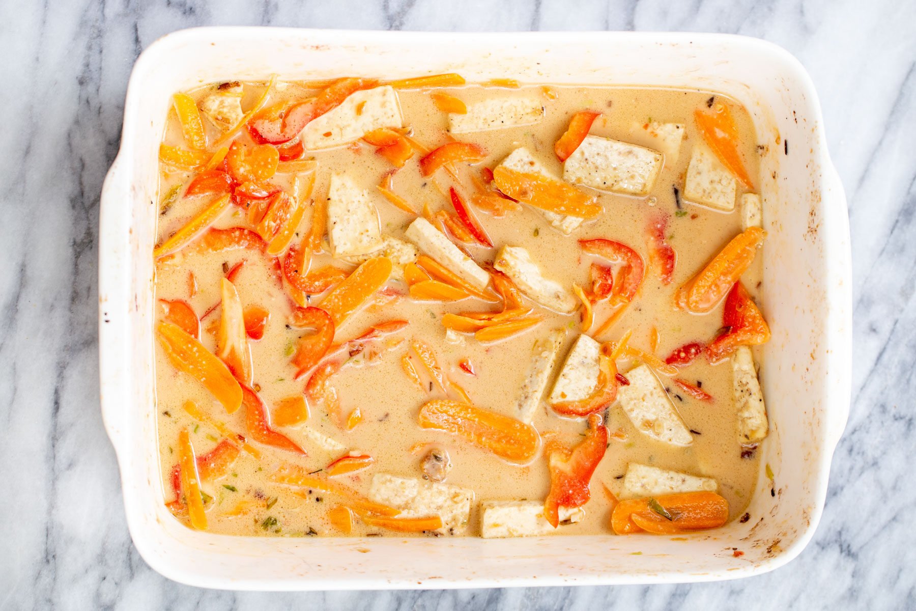 coconut milk being added to a casserole dish with veggies and tofu
