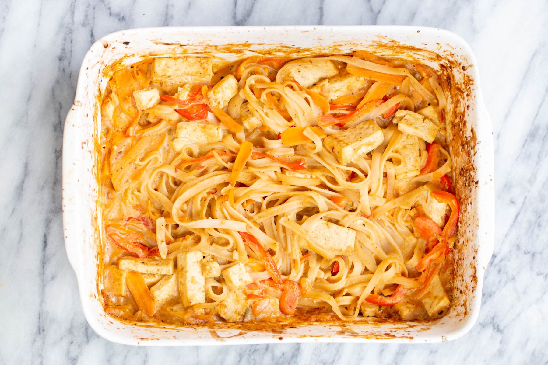 peanut rice noodles rice noodles being combined with creamy peanut butter sauce in a casserole dish