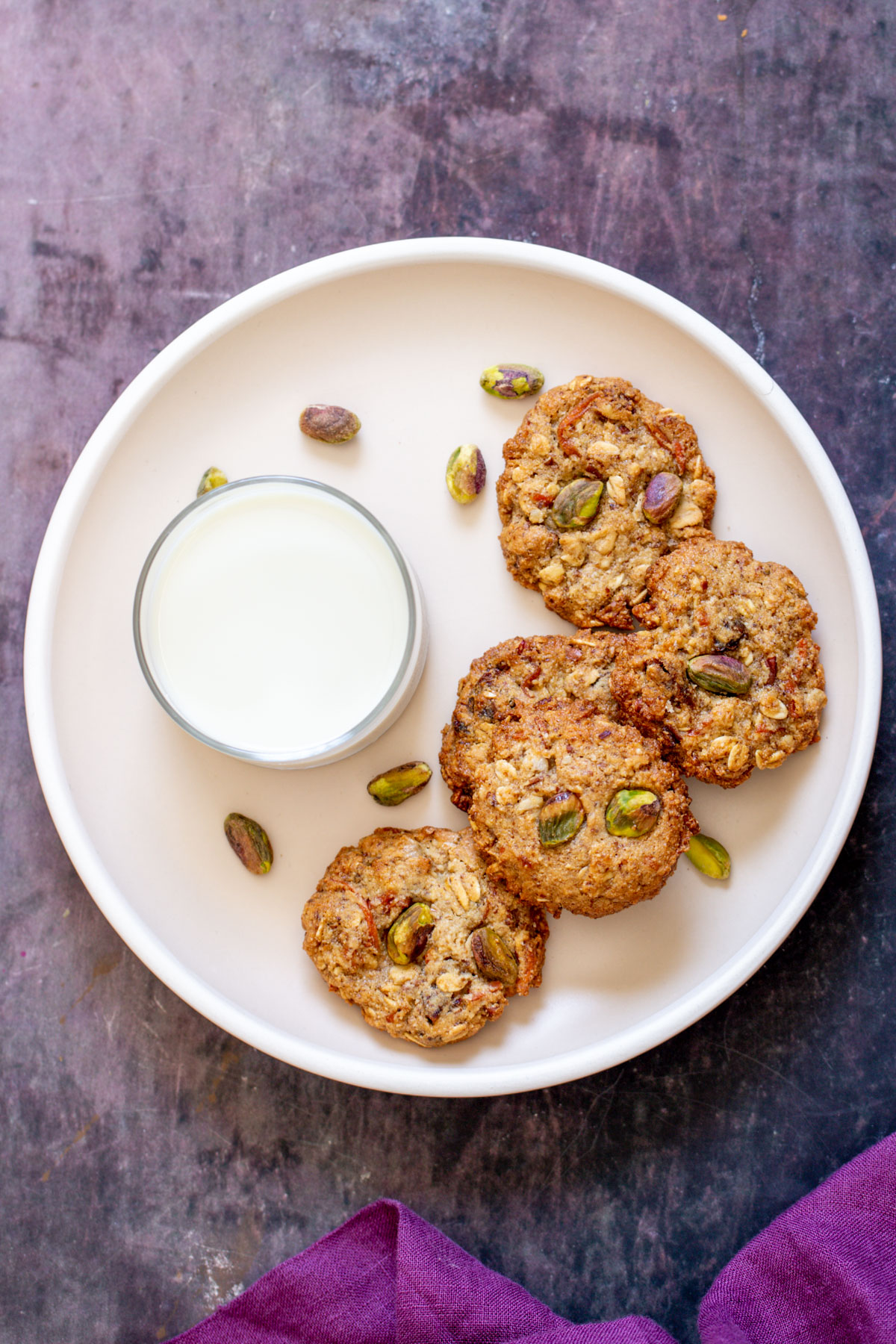 a small white plate with a glass of milk and three carrot cake cookies