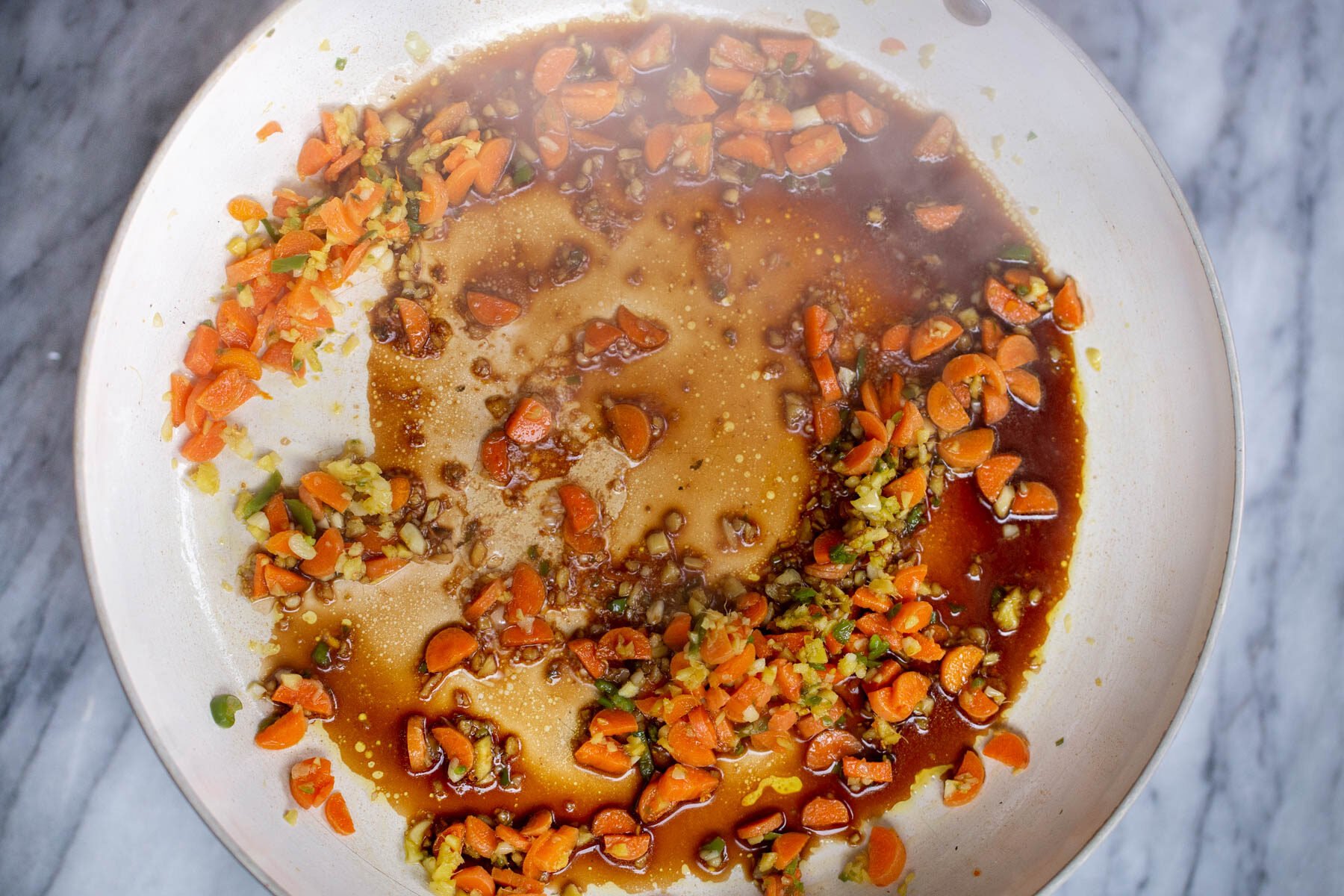 sauce being added to a pan with carrots, ginger and garlic