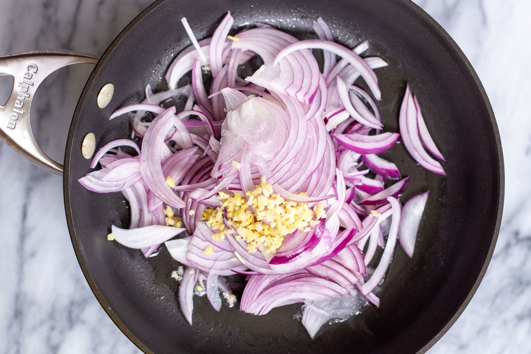 sliced red onions and ginger in a black sauteeing pan