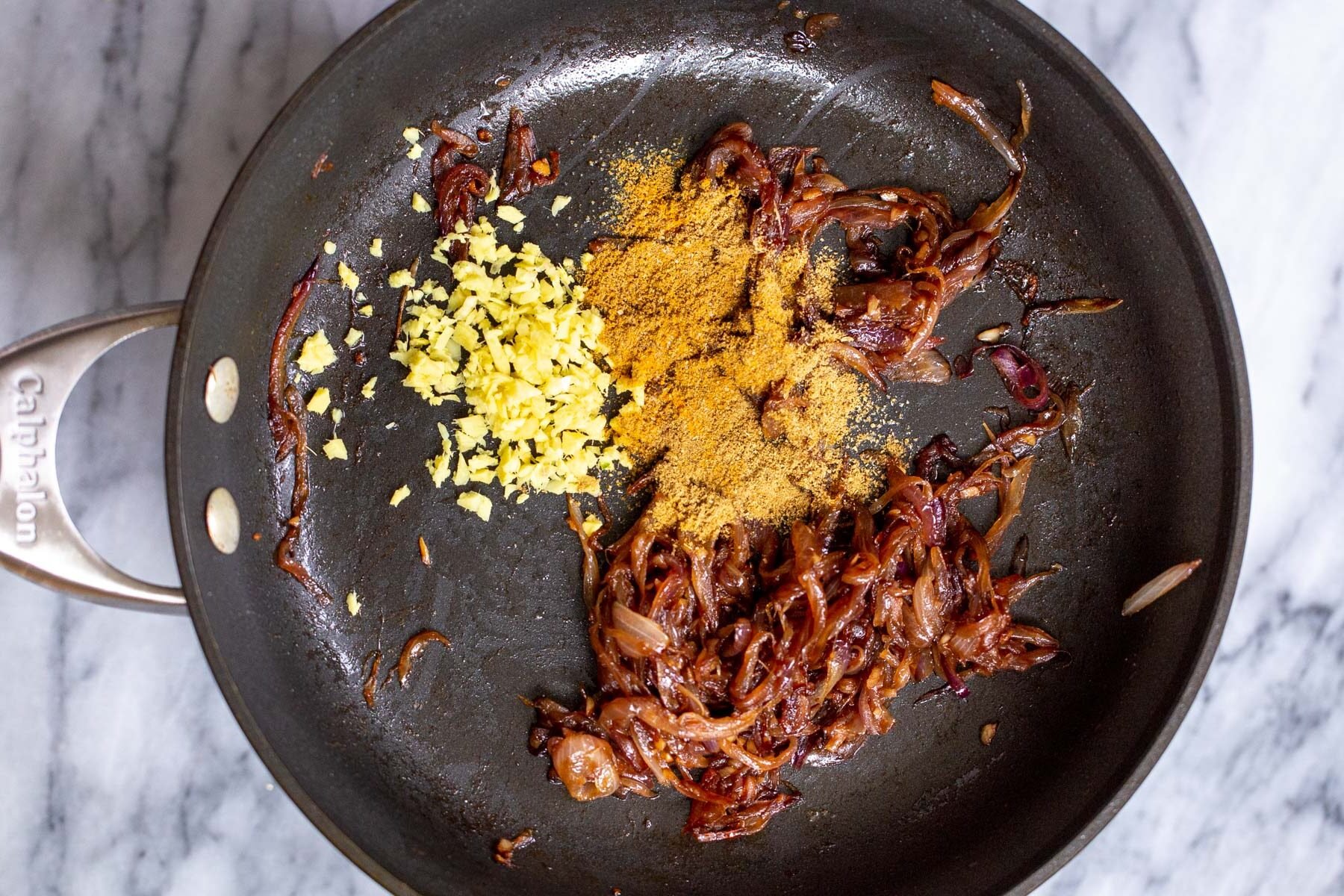 dried spices and ginger being added to sauteed onions in sauteeing pan