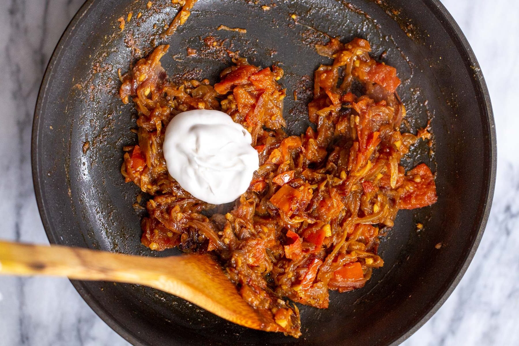 coconut yogurt being added to tempered onions and spices in sauteeing pan