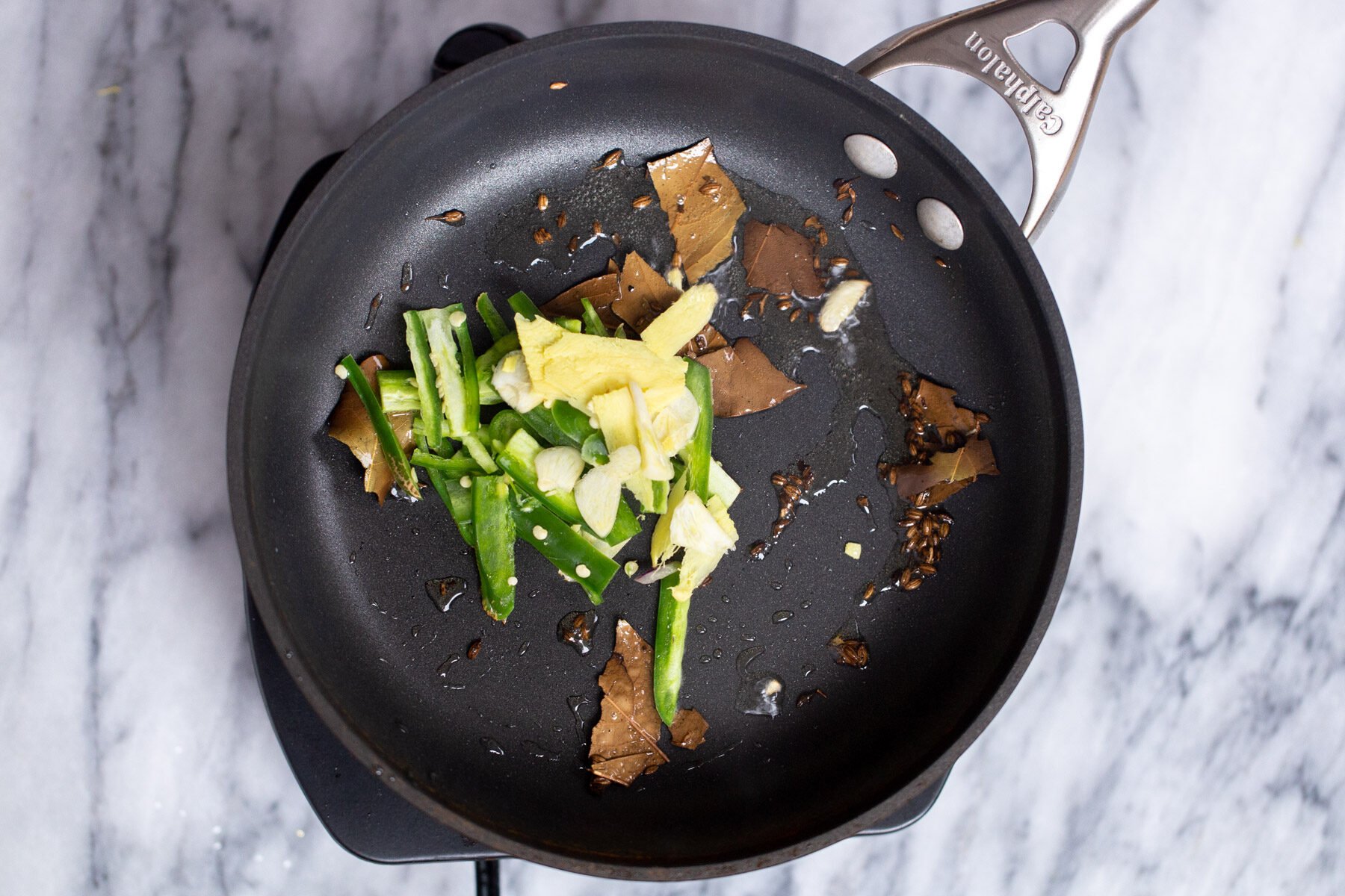 ginger and green chile being added to sauteeing pan with hot oil