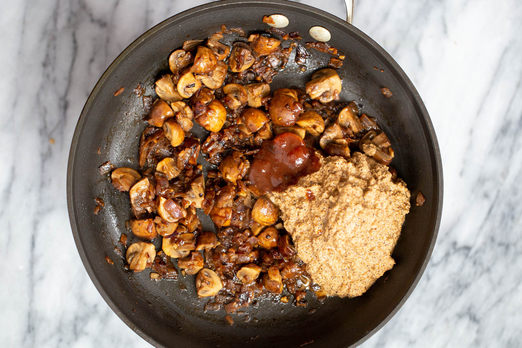 xacuti spice paste being added to mushrooms in a sauteeing pan