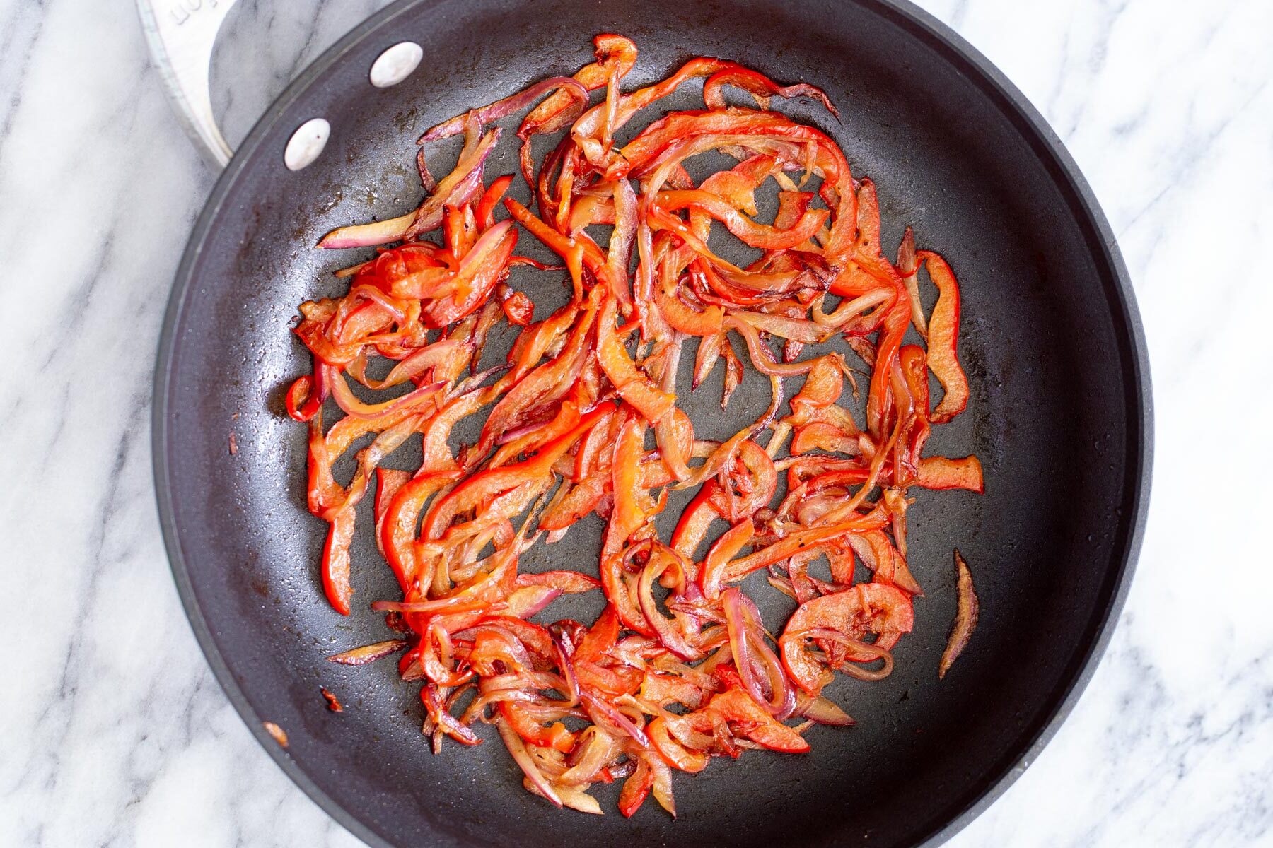 red bell peppers being sauteed in a frying pan