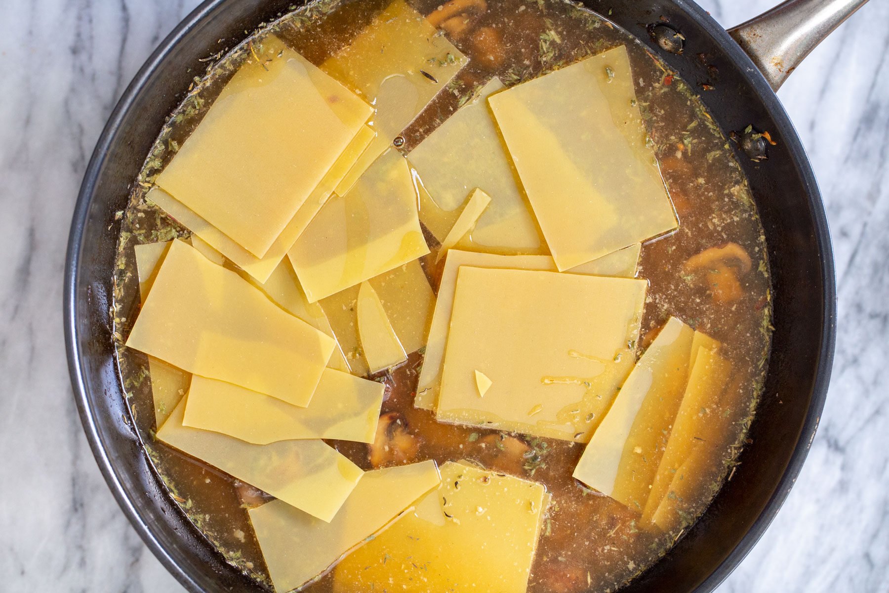 broken lasagna noodles being added to a skillet with mushroom broth