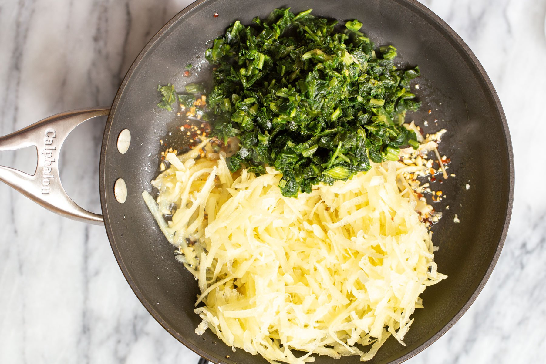 grated potatoes, chili flakes and spinach in a skillet