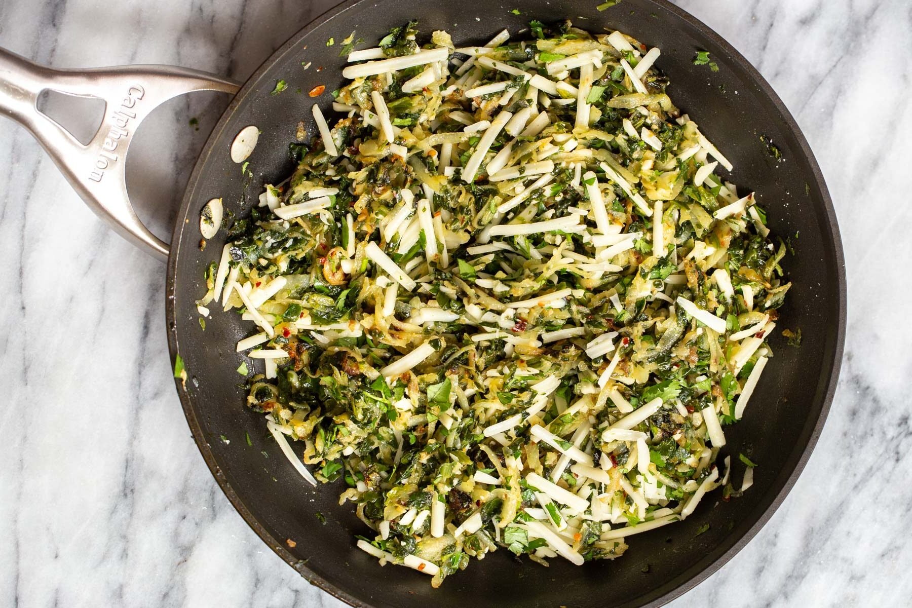 vegan mozarella being added to spinach potato filling in a skillet