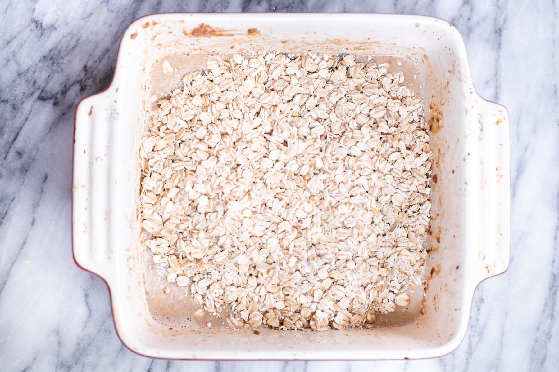 rolled oats being added to casserole dish with banana batter