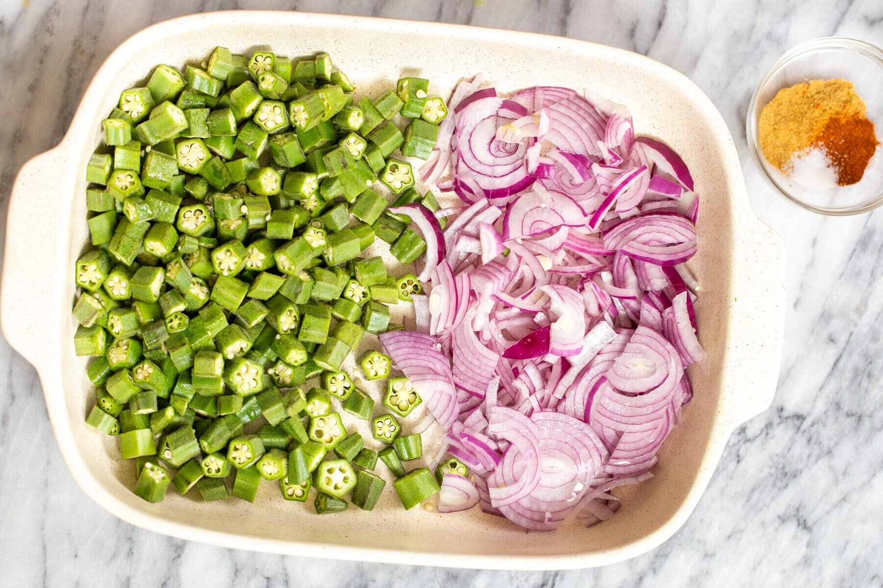 raw sliced okra and onion in a white casserole dish