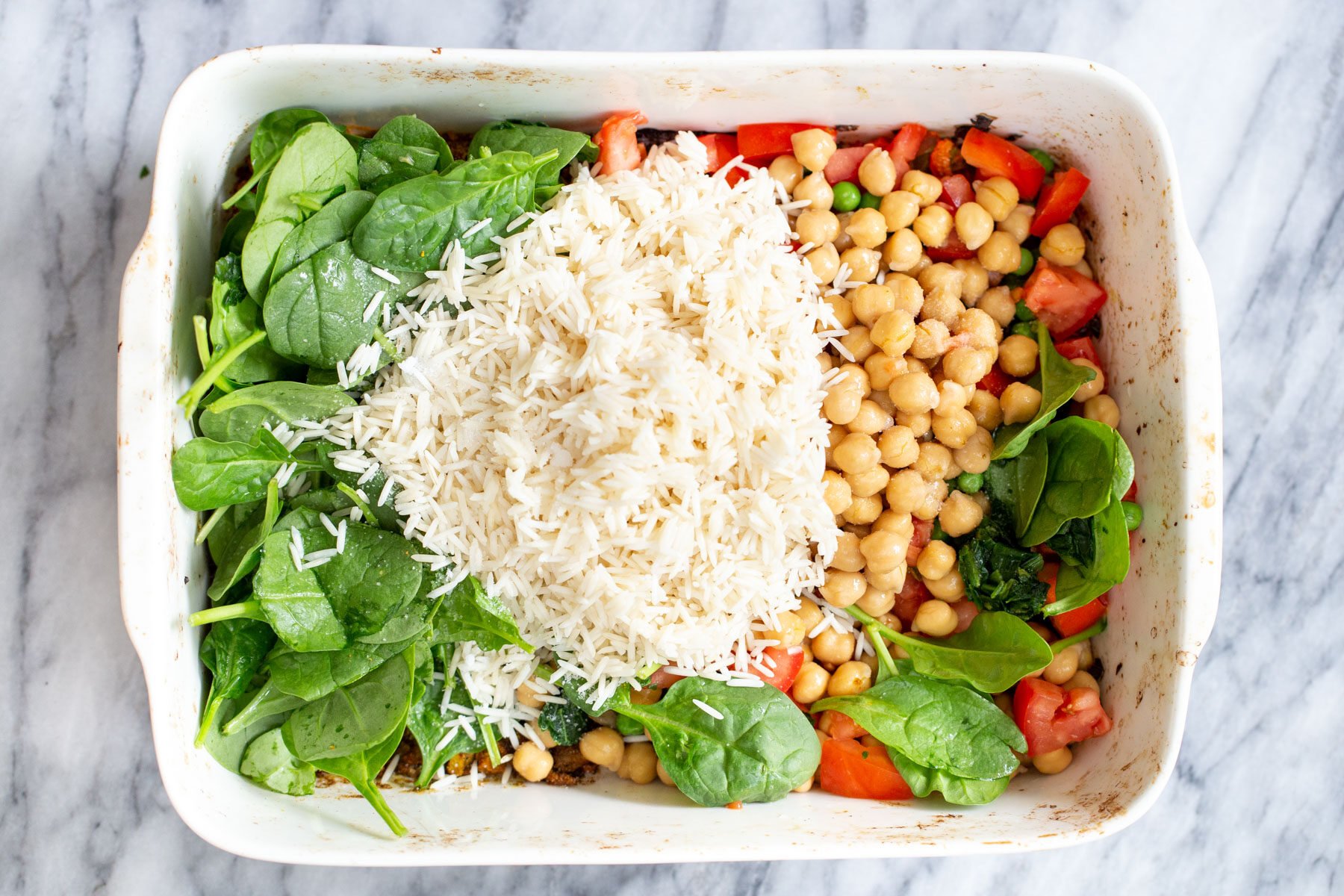 drained soaked rice, chickpeas, and spinach being added to vegetables in a white casserole