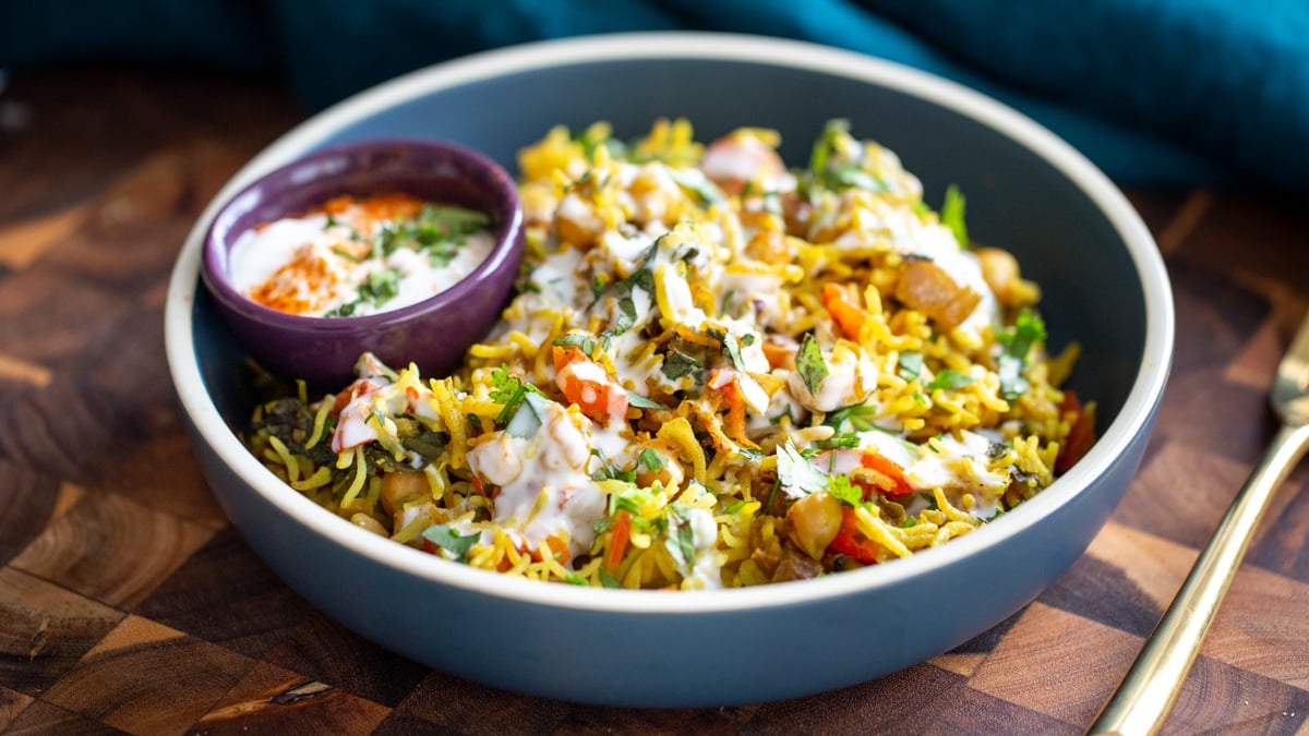 side view of a blue bowl with chickpea rice pulao drizzled with raita