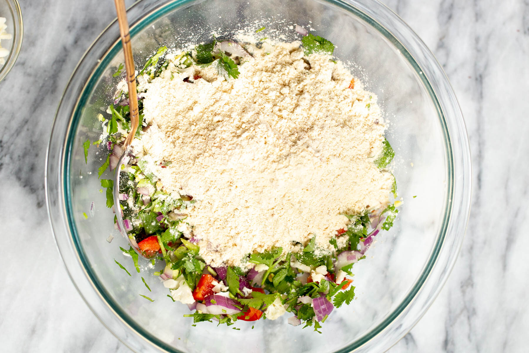 chickpea flour being added to chopped veggies in a bowl