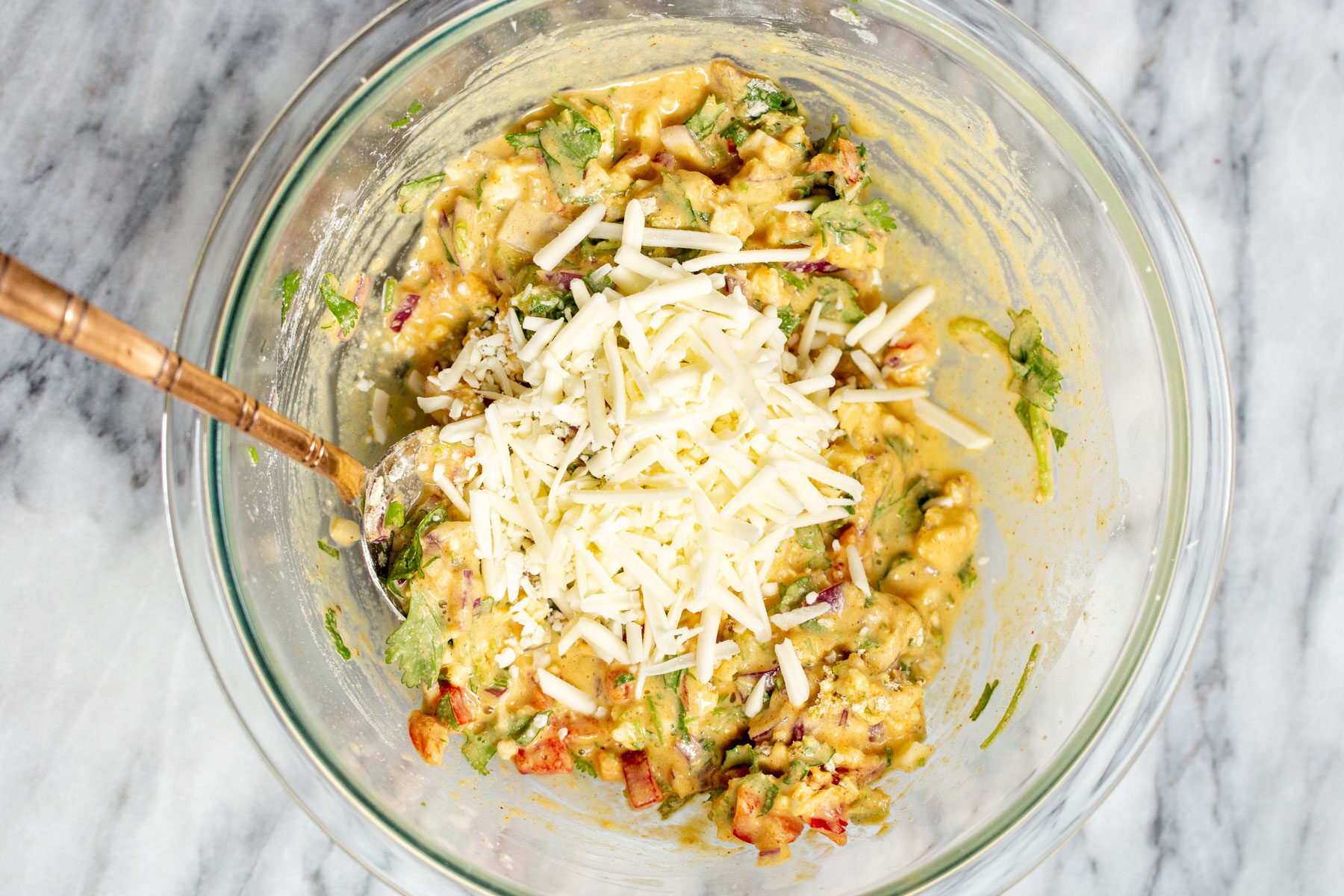 shredded vegan cheese being added to pancake batter in a glass bowl