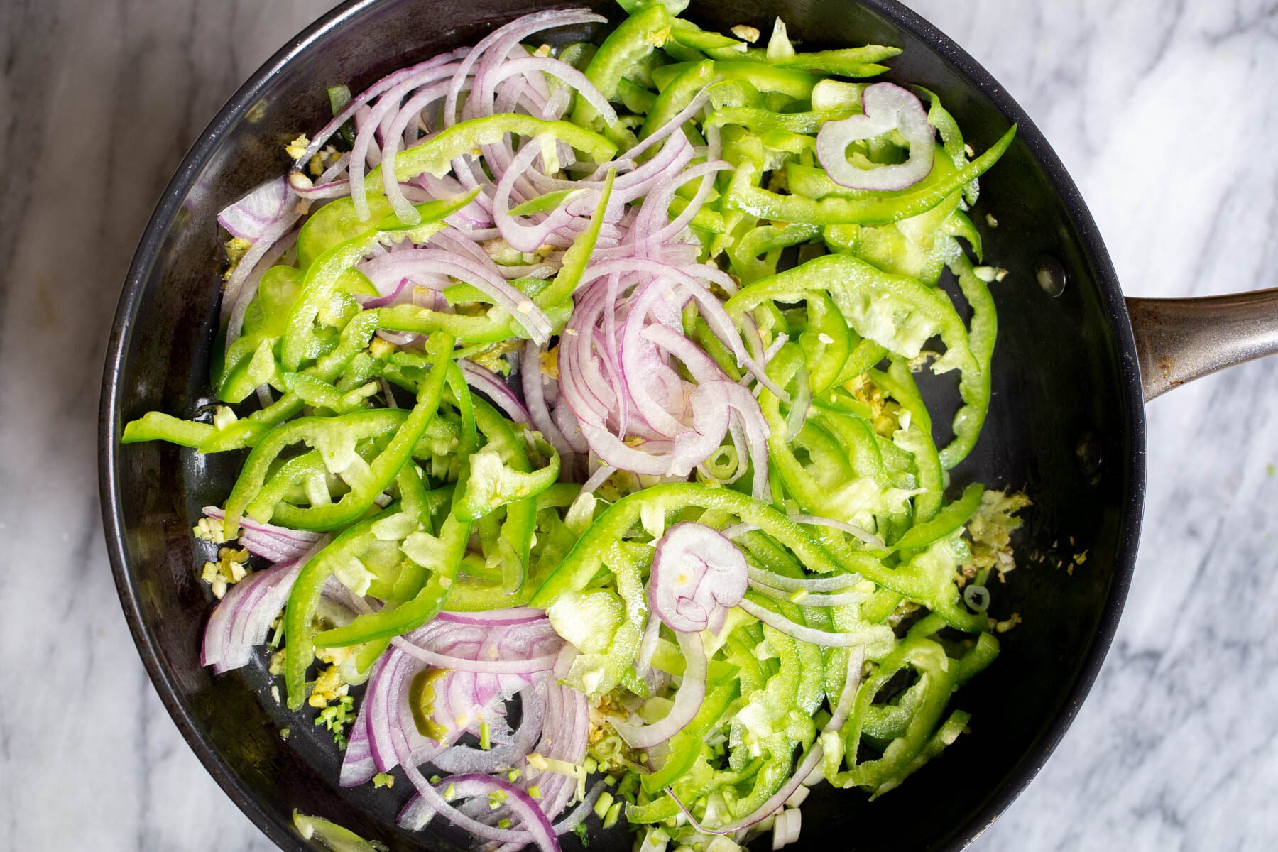 sliced onion and green chili in a black sauteeing pan