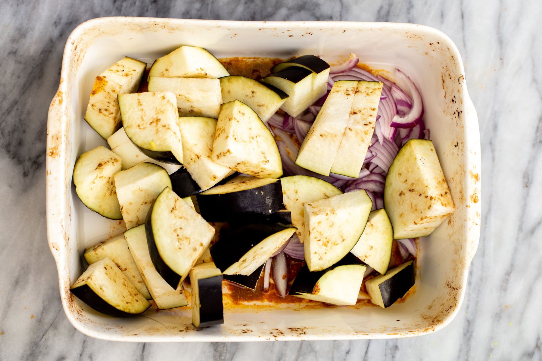eggplants and onion slices in a white casserole dish