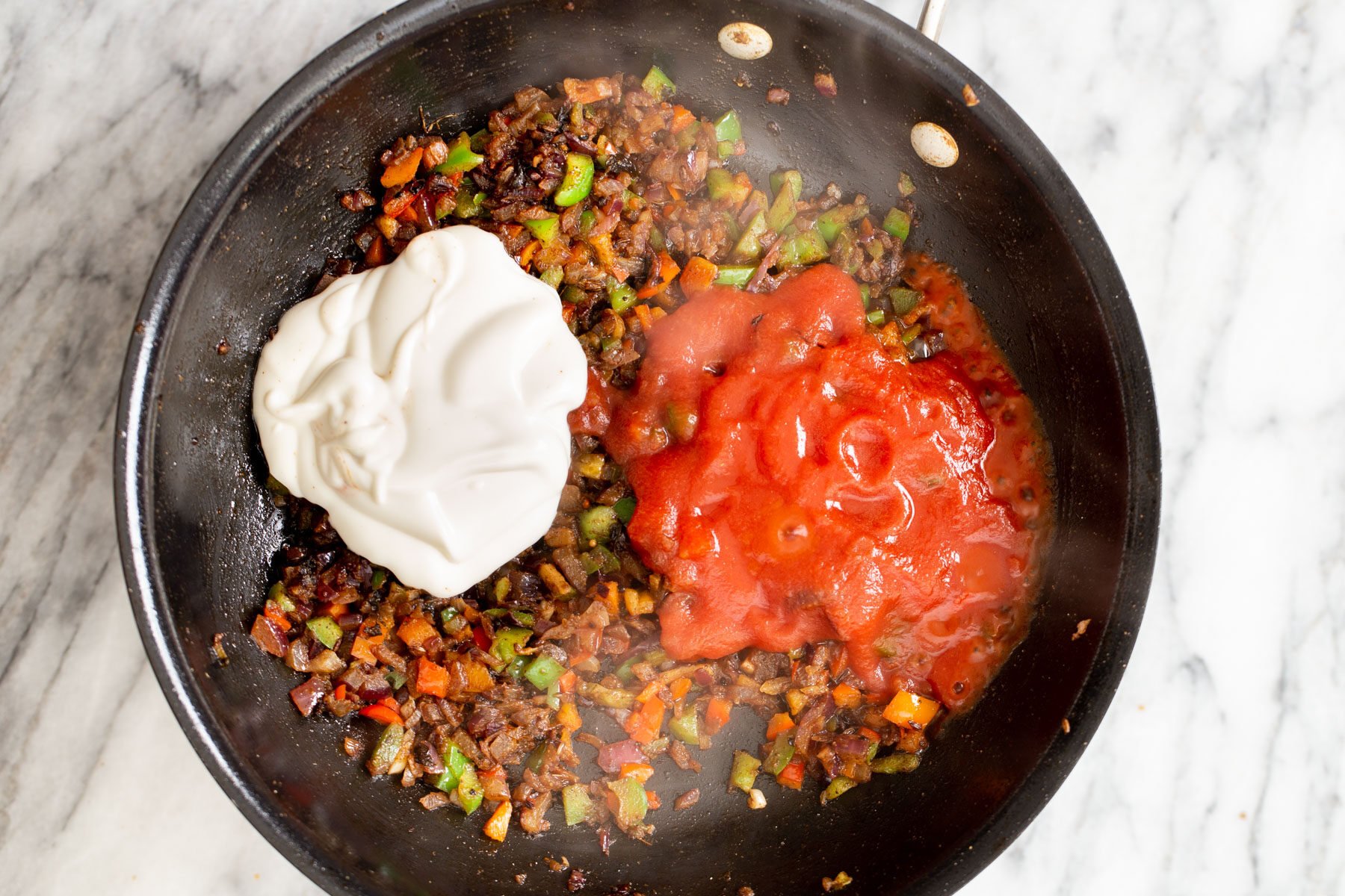 cashew cream and tomatoes being added to a skillet