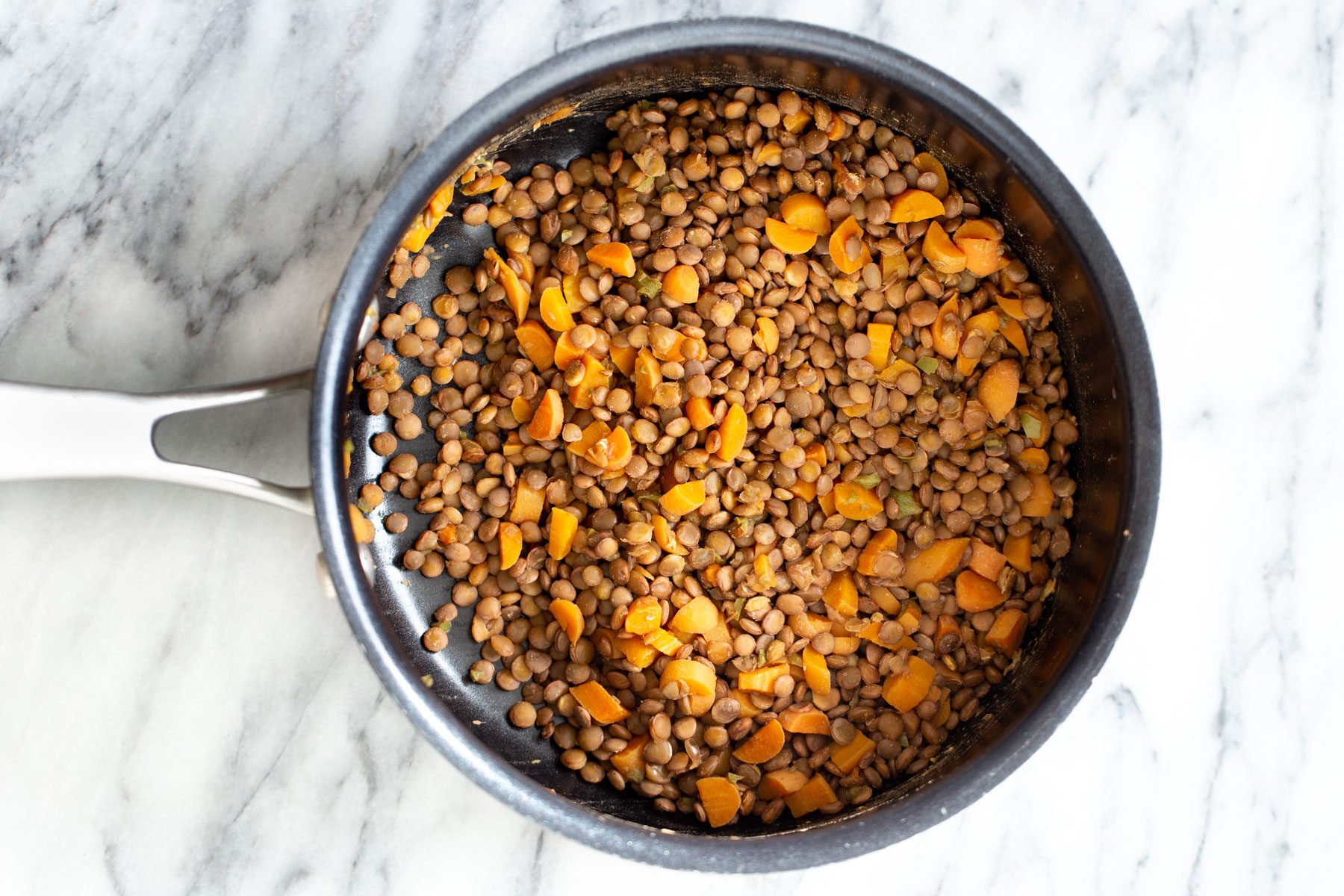 cooked brown lentils and carrots being added to a skillet