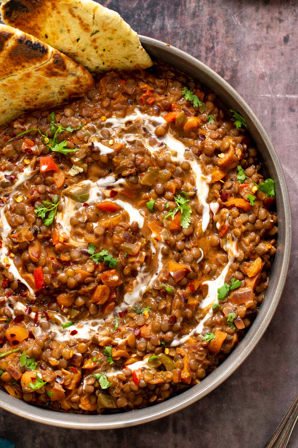 a bowl if vegan Indian lentil curry served with a drizzle of cashew cream and naan