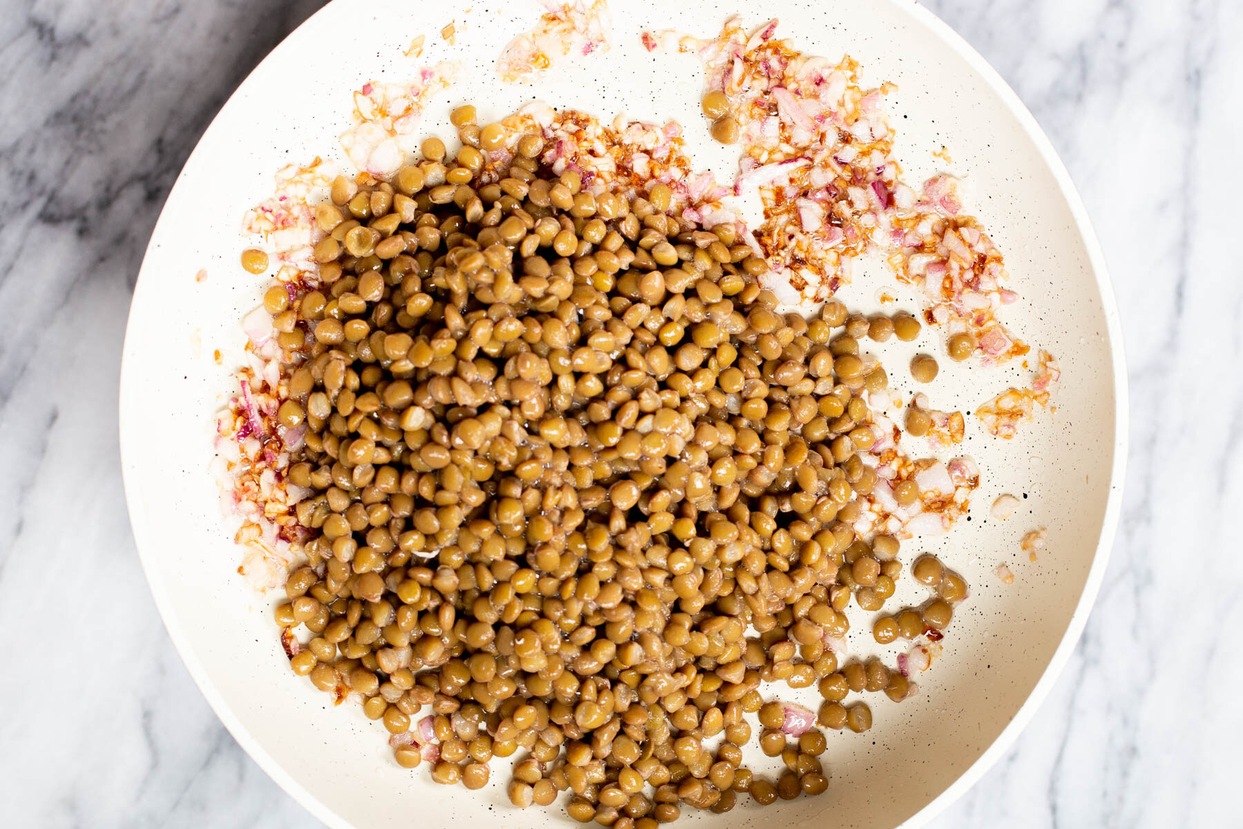 brown lentils and diced onions in a white sauteeing pan