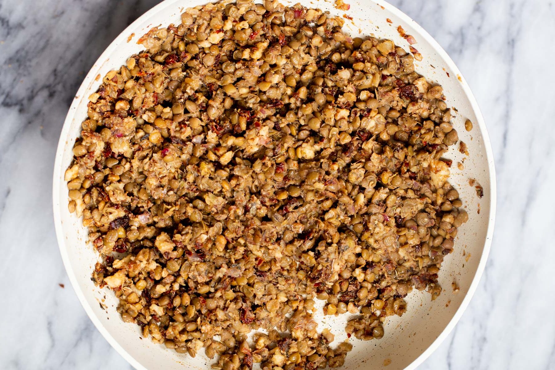 mashed lentils and sauteed onions in a white sauteeing pan 