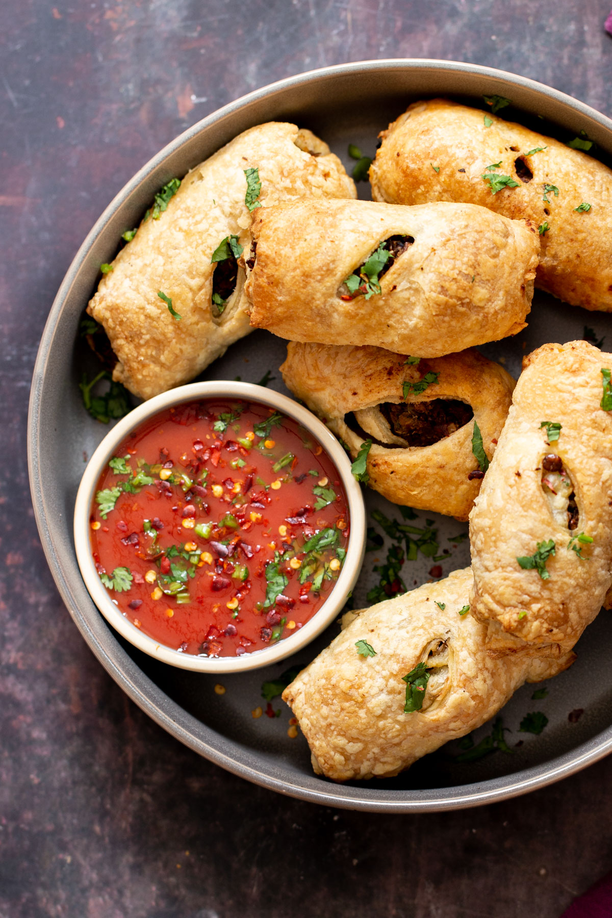 a platter with vegan sausage rolls next to a small dish with tomato sauce