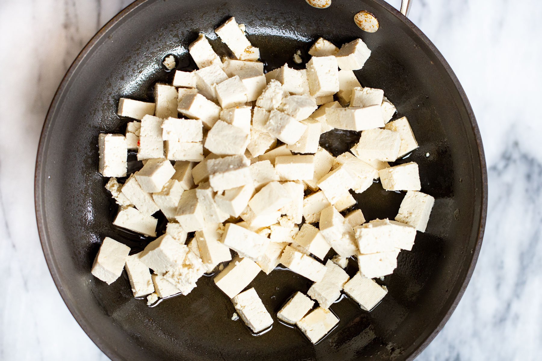 tofu cubes frying in a black skillet