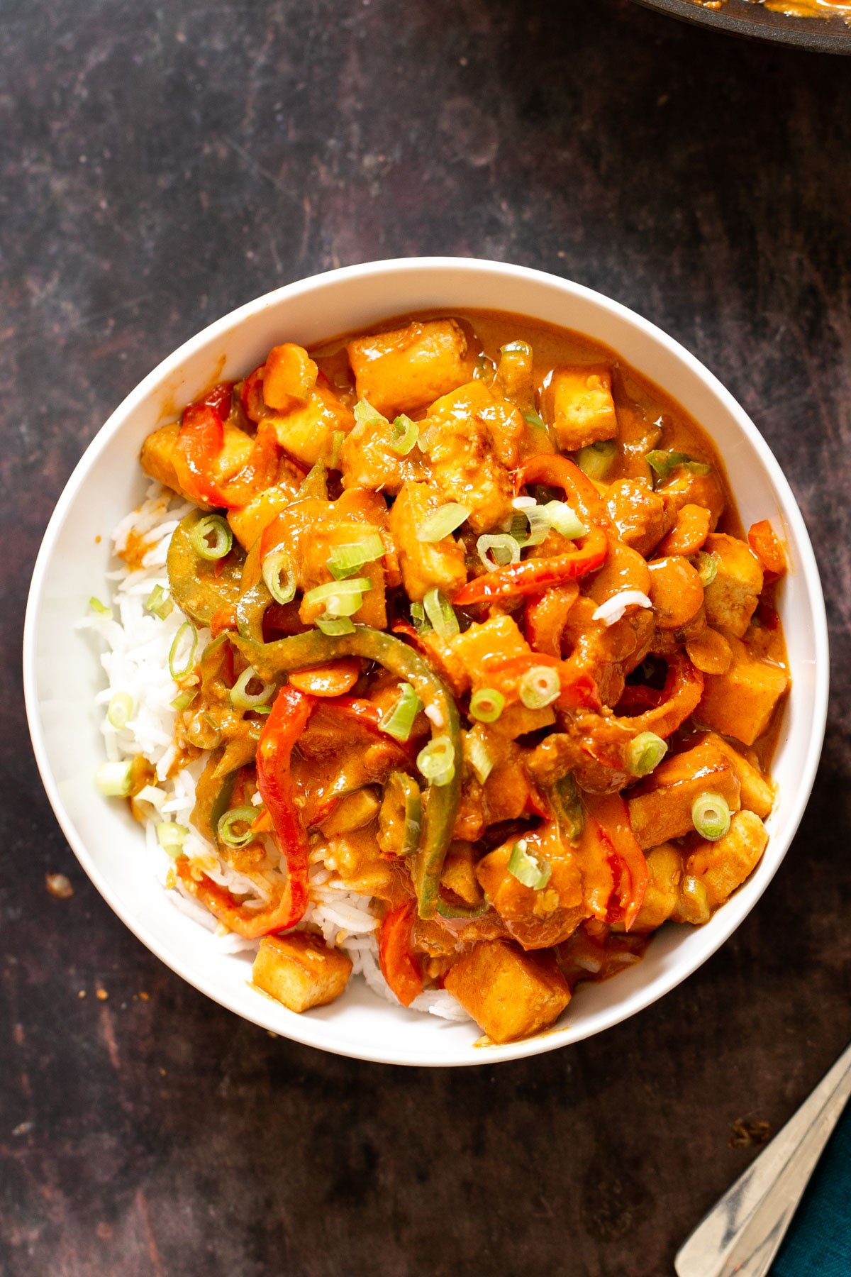 a bowl of gochujang tofu stir-fry served over rice in a white bowl