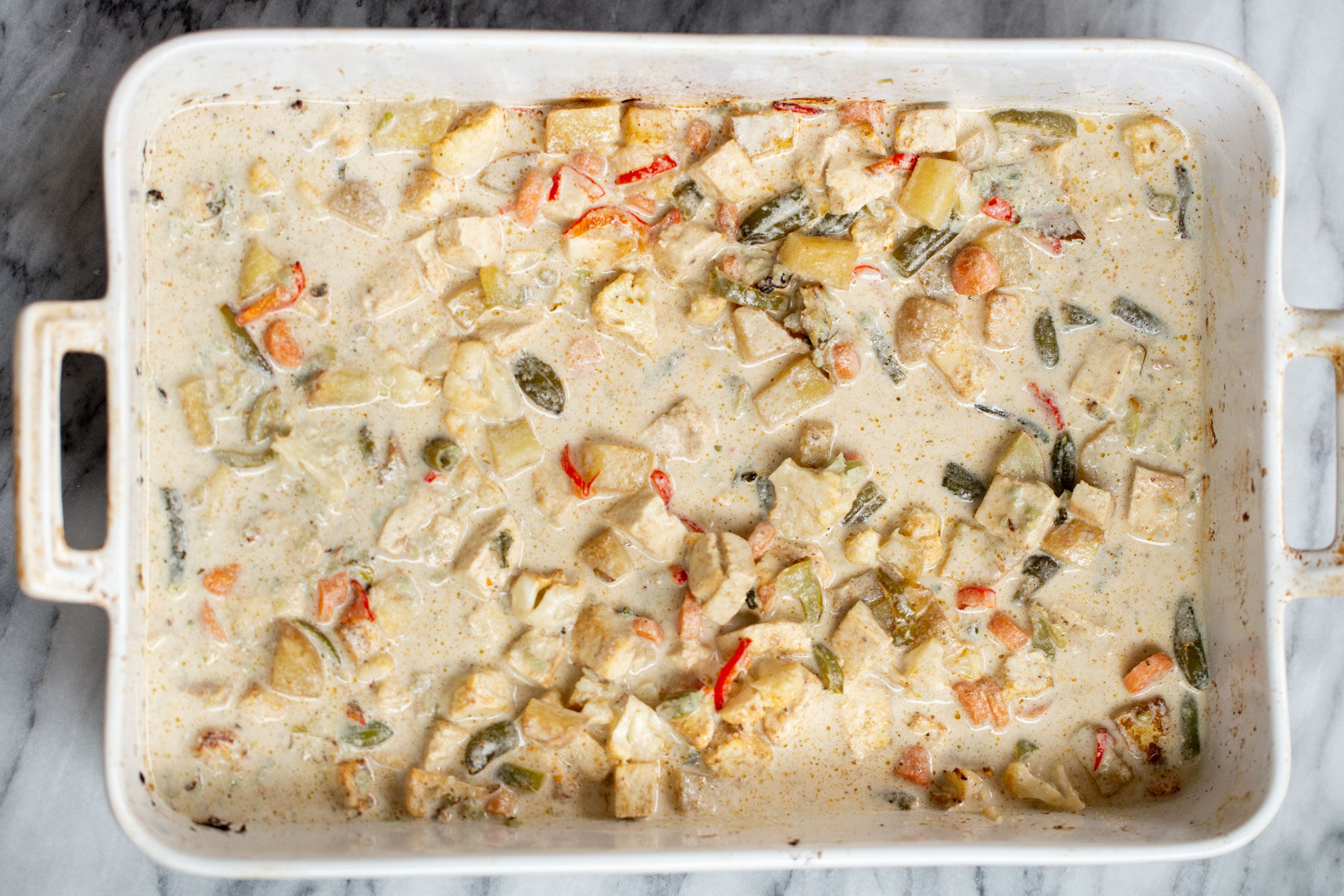 Navratan Korma creamy cashew sauce being poured on top of roasted veggies