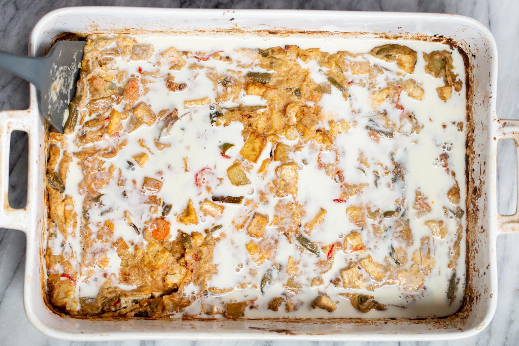 Navratan Korma  milk being added to tofu and veggies in a white casserole dish