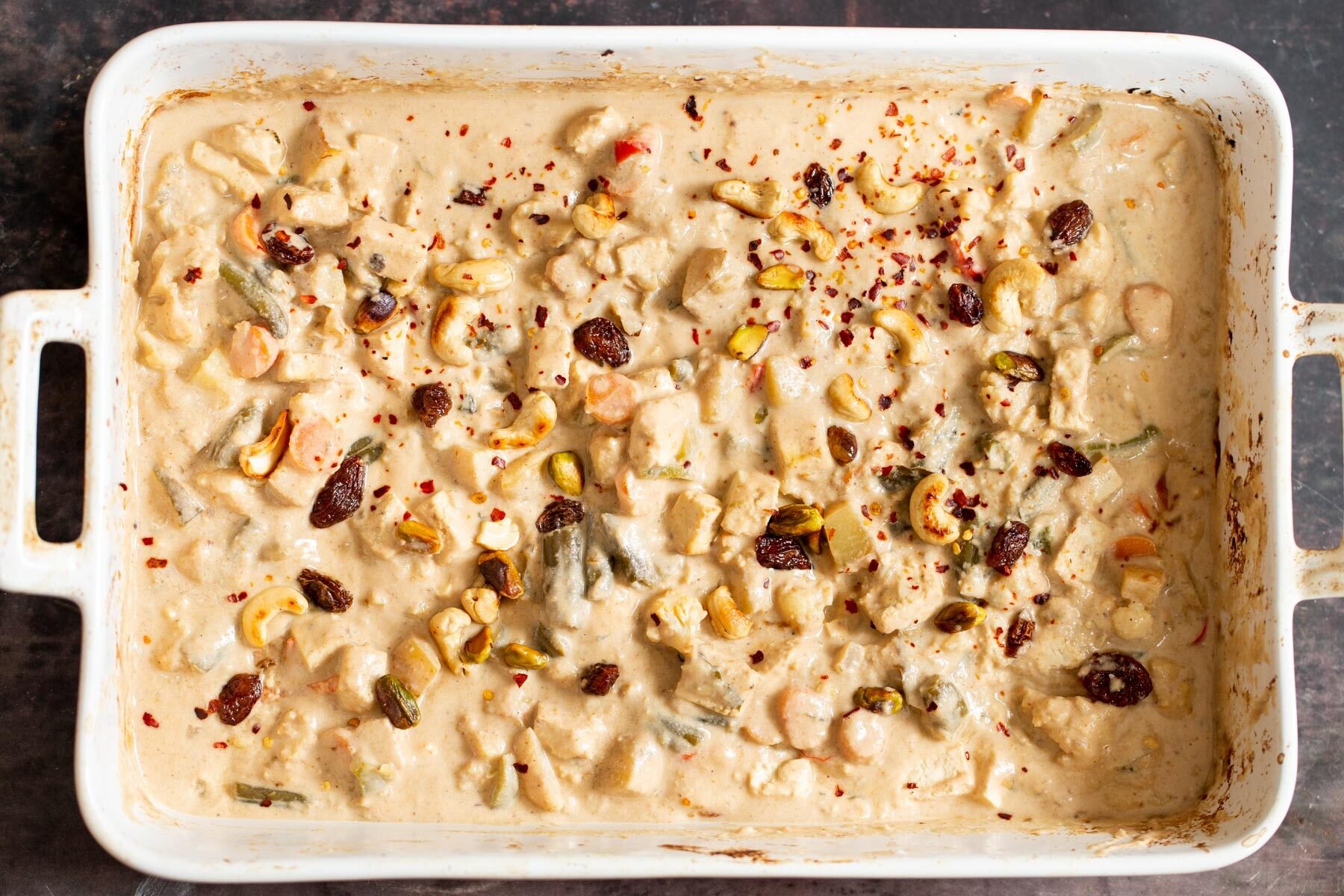 creamy Indian Navratan Korma curry in a white casserole dish sprinkled with nuts and chili flakes