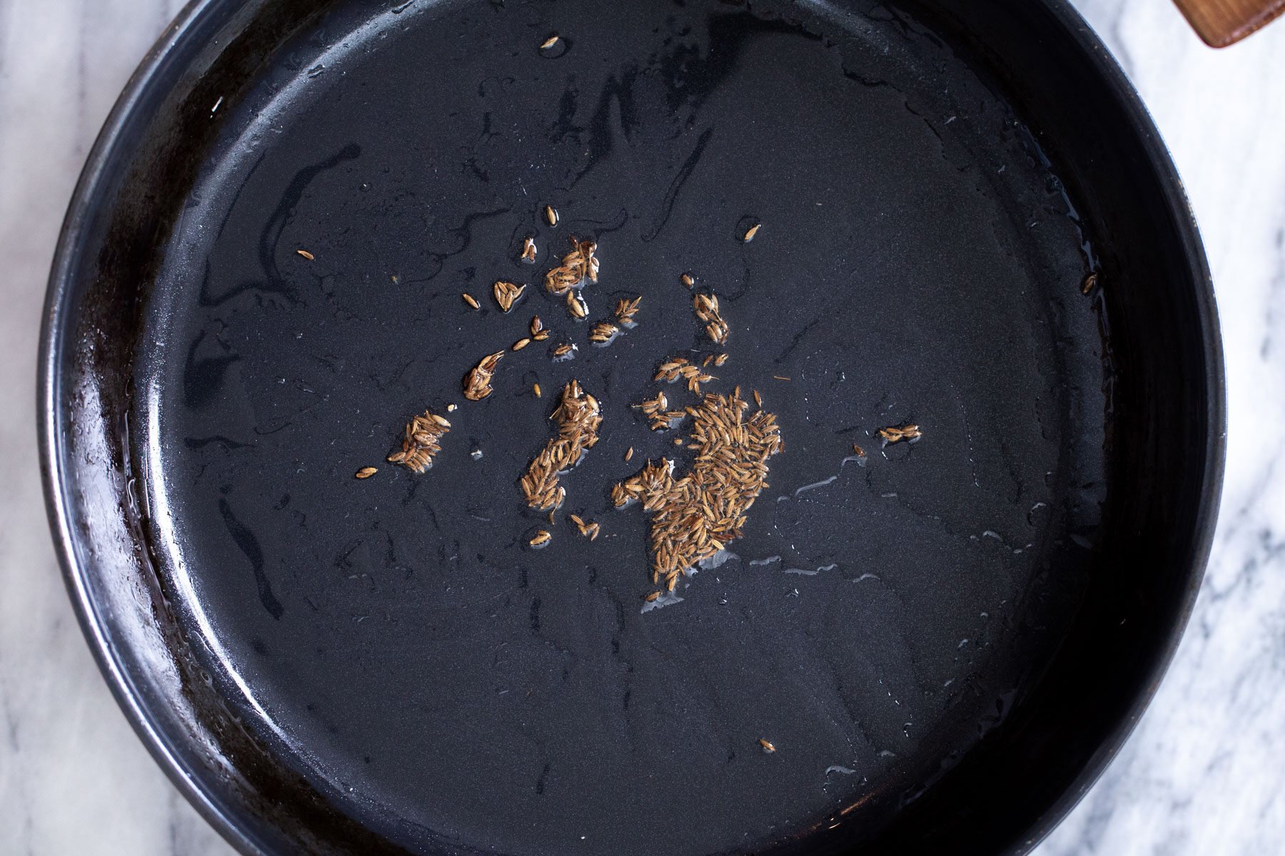 cumin seeds in a black sauteeing pan