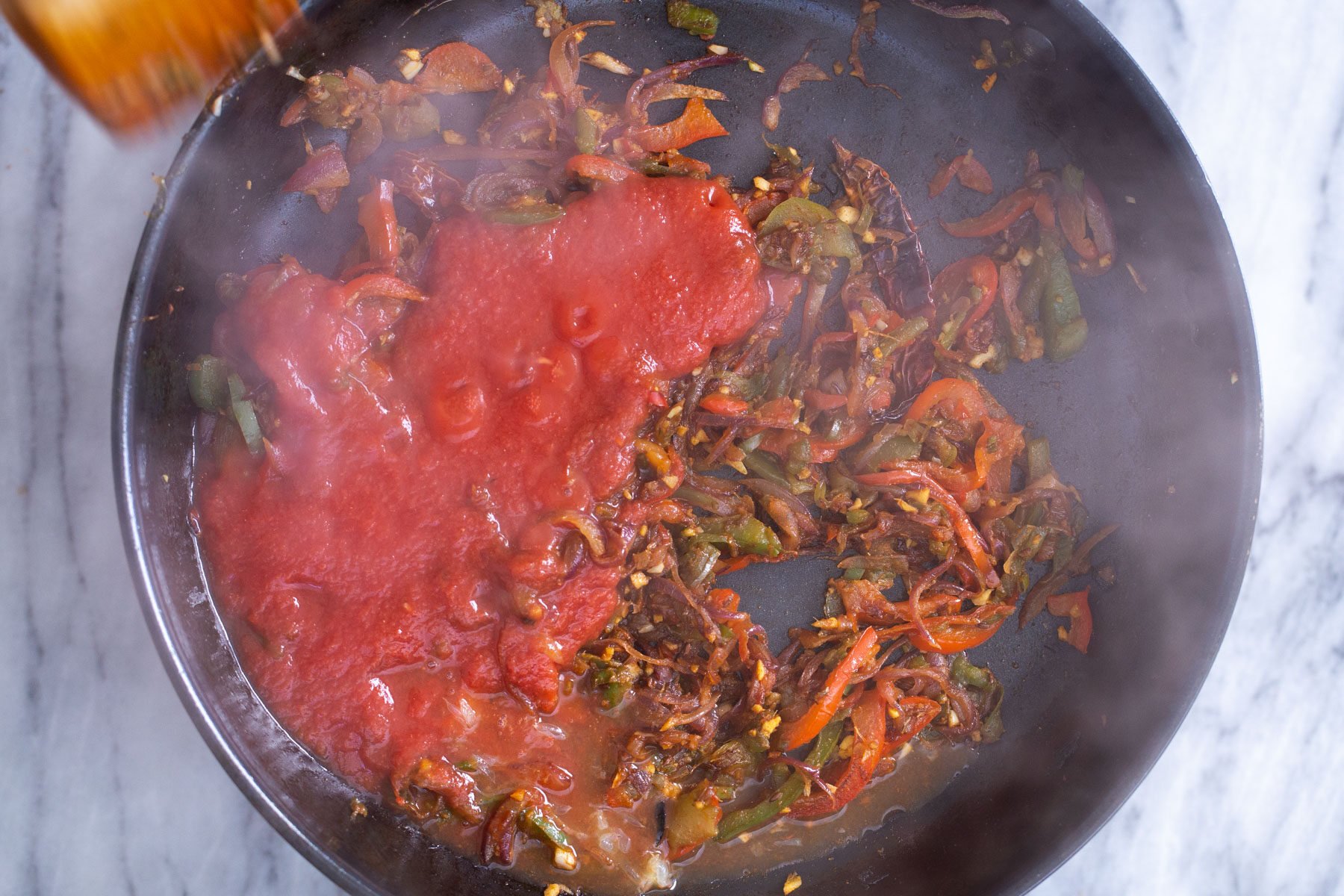 tomato sauce being added to skillet with bell pepper and spices
