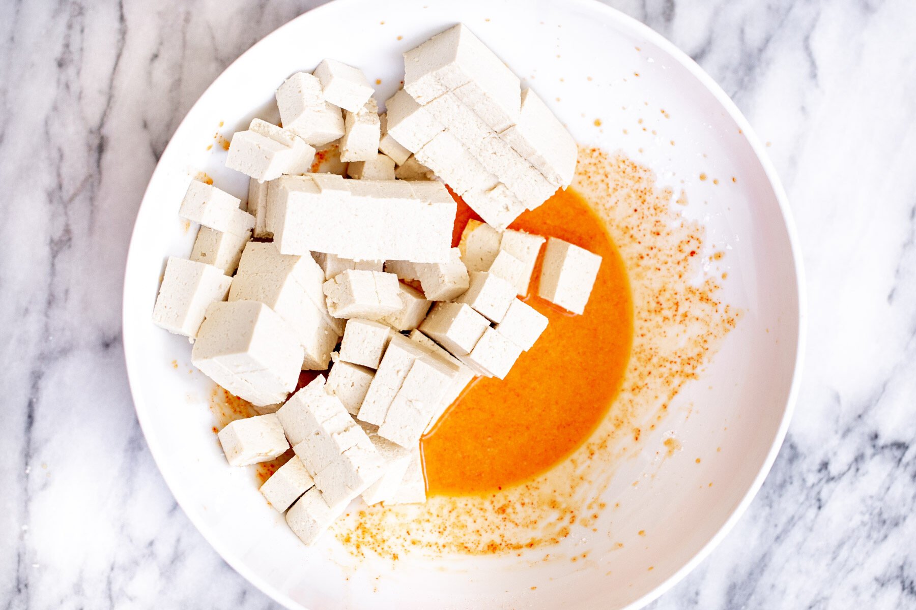 tofu cubes on a white plate mixed with spices and cornstarch