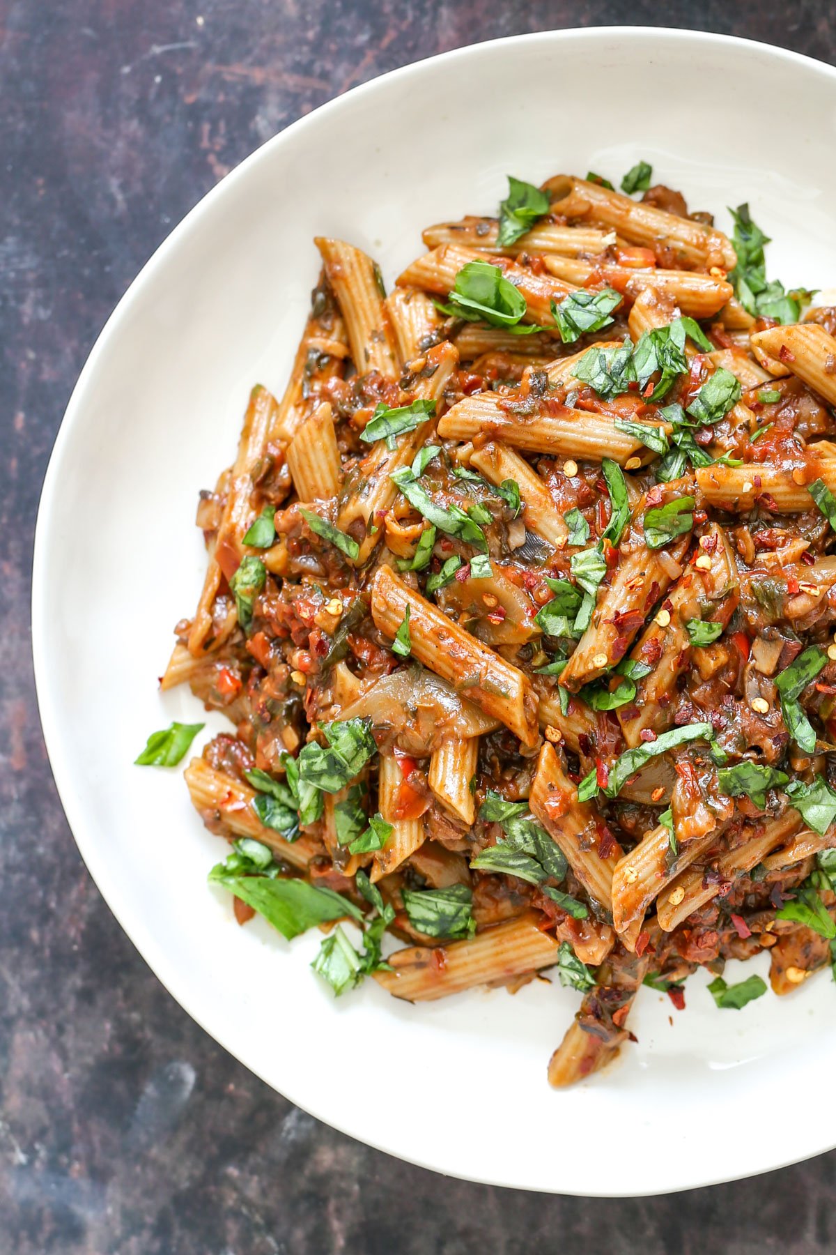 a white plate with penne with walnut sun-dried tomato sauce and fresh basil