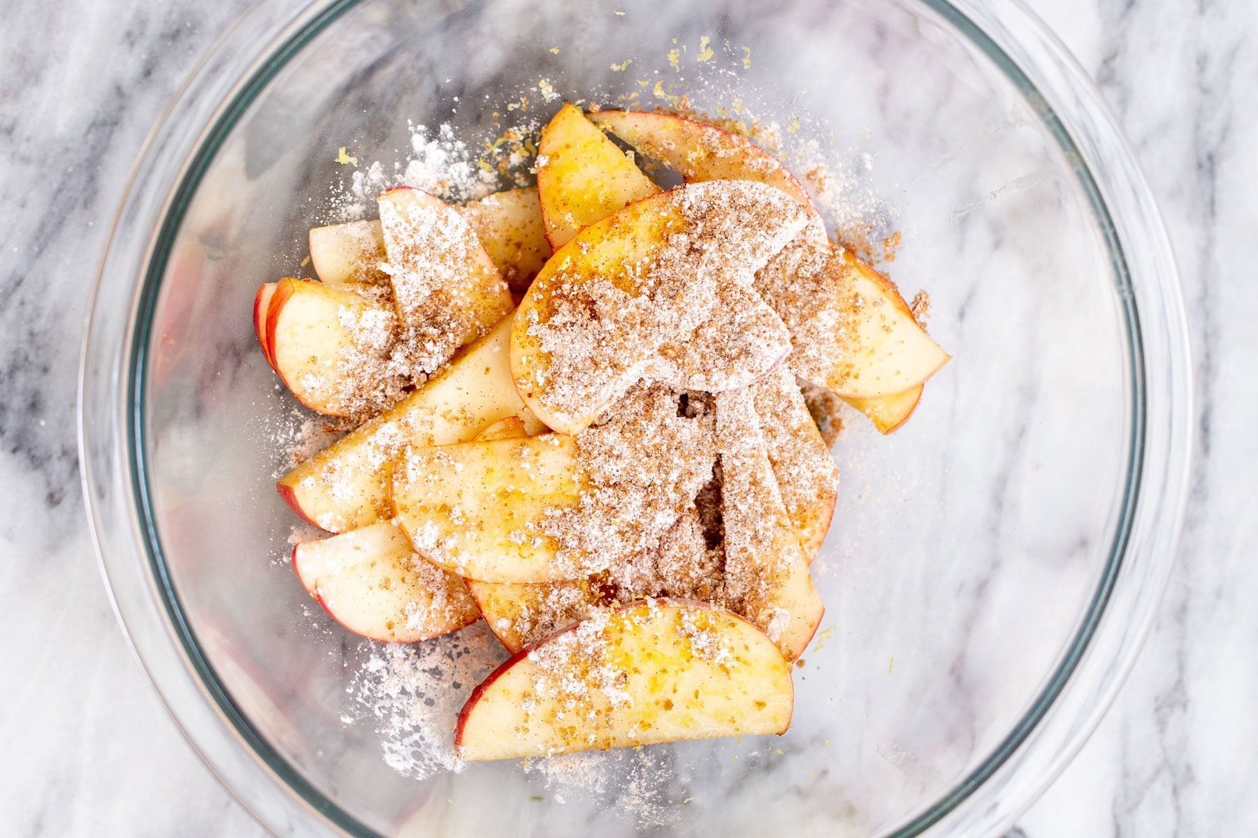apple slices in a glass bowl being mixed with brown sugar and cornstarch