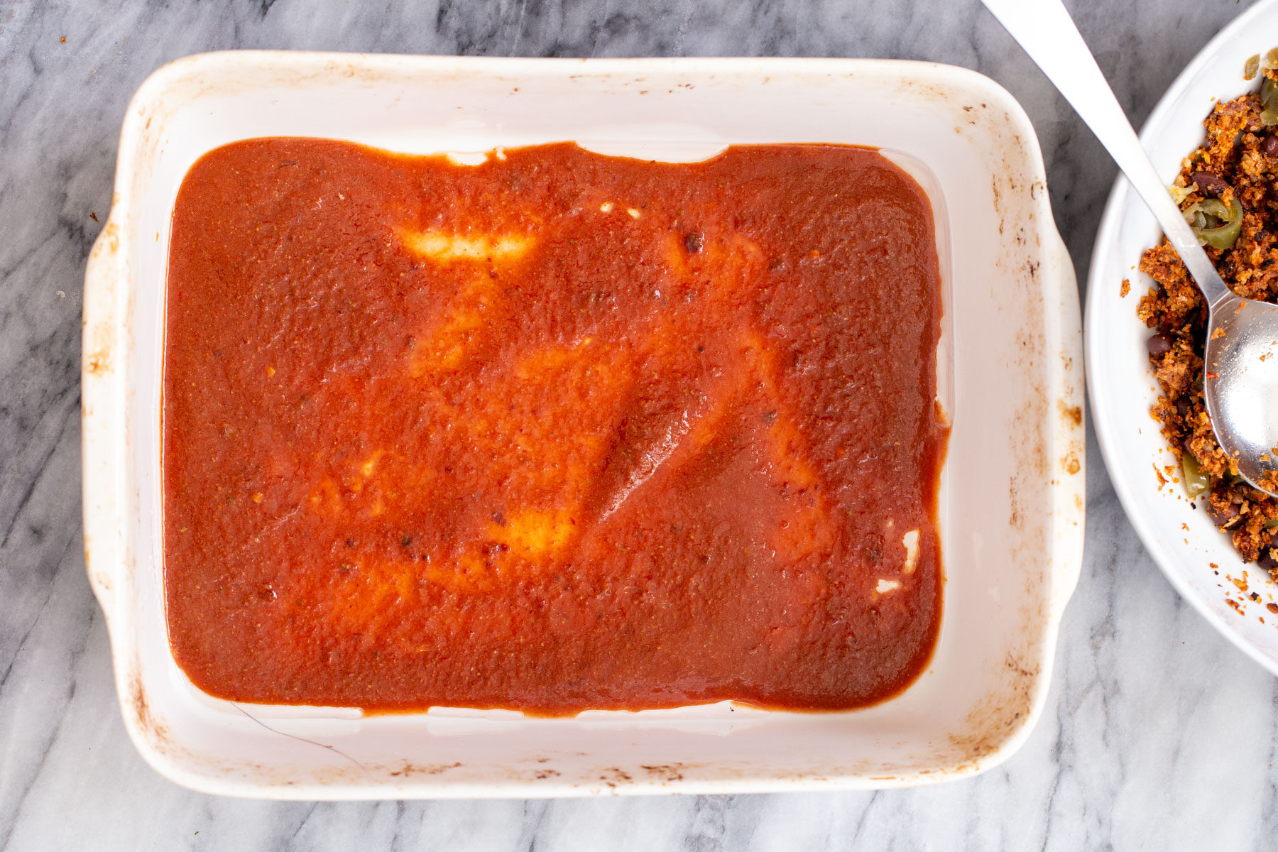 vegan enchilada sauce being added to casserole dish