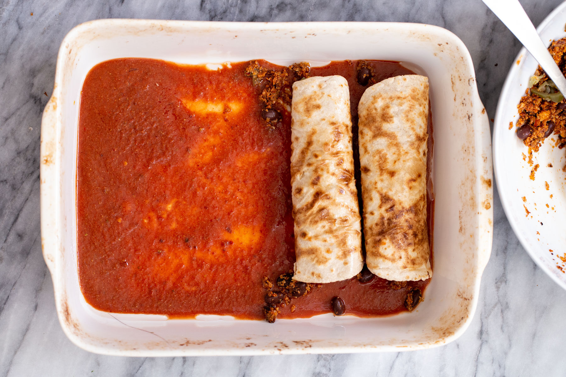 enchiladas being filled and added to a casserole dish