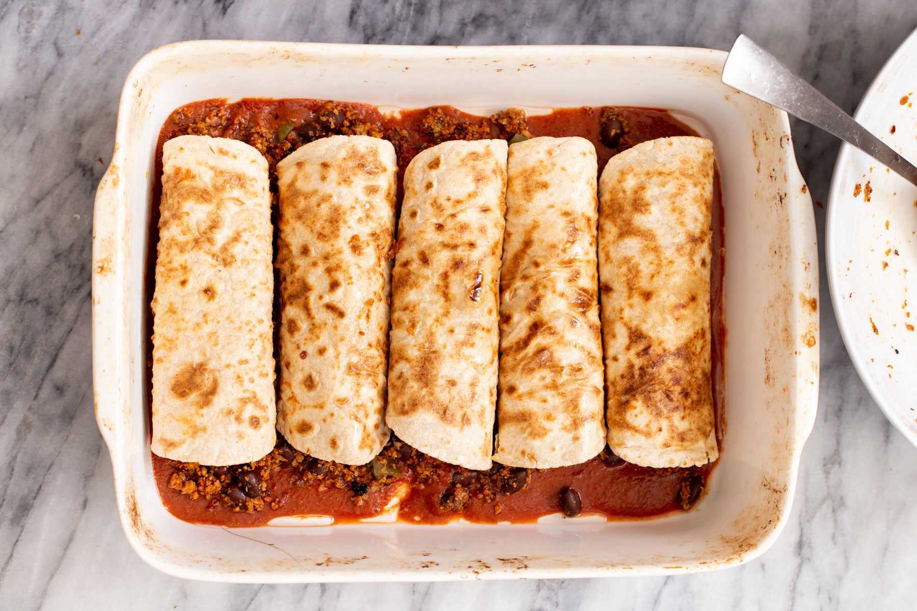 a casserole dish with rolled up enchiladas in tomato sauce