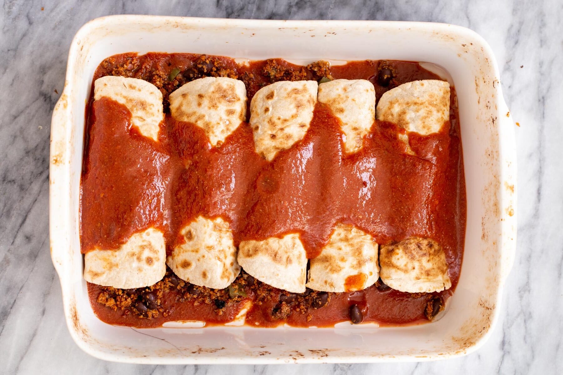 vegan taco meat stuffed enchiladas in a casserole dish covered with red salsa
