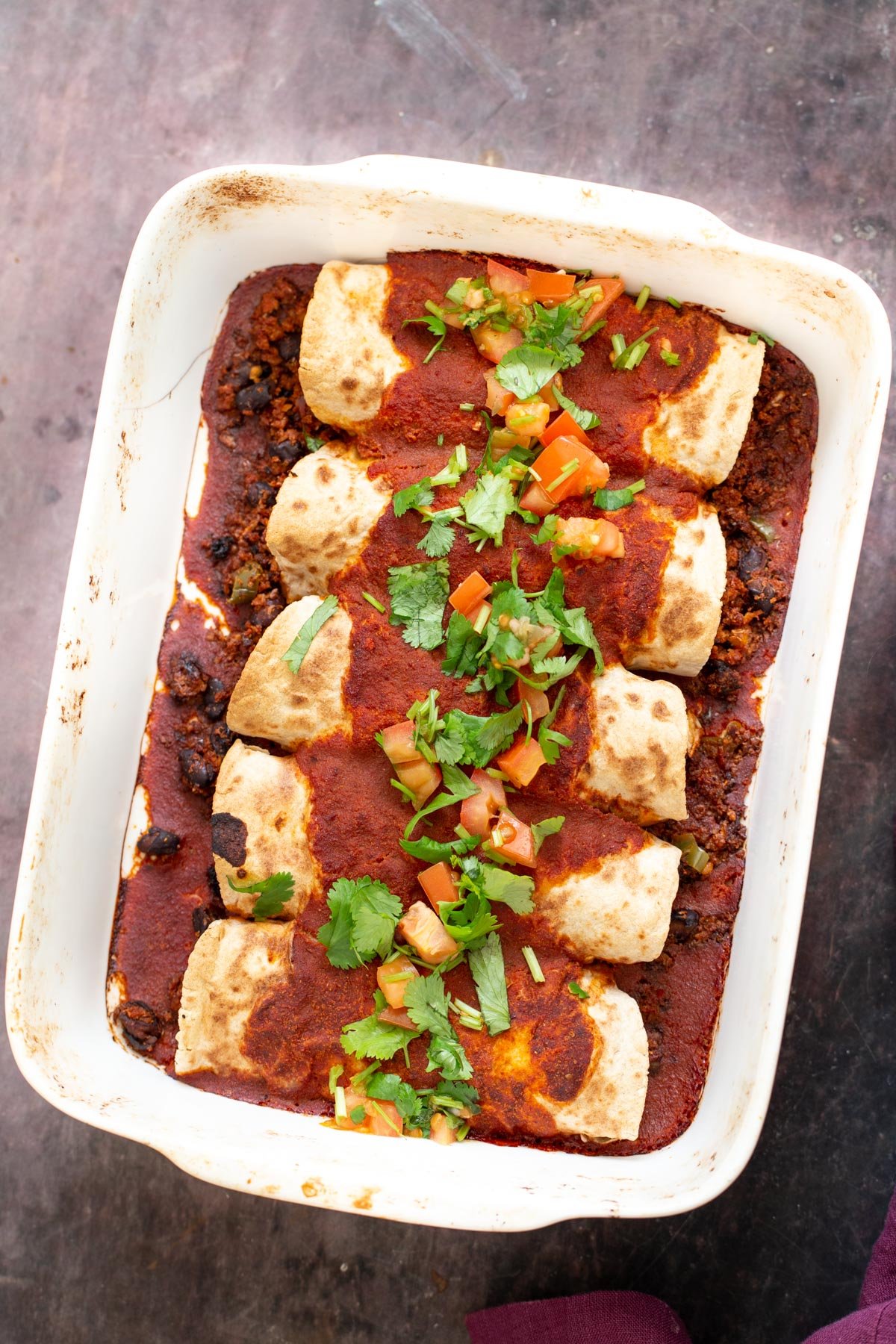 vegan enchiladas filled with cauliflower taco meat and topped with homemade enchilada sauce in a white casserole dish