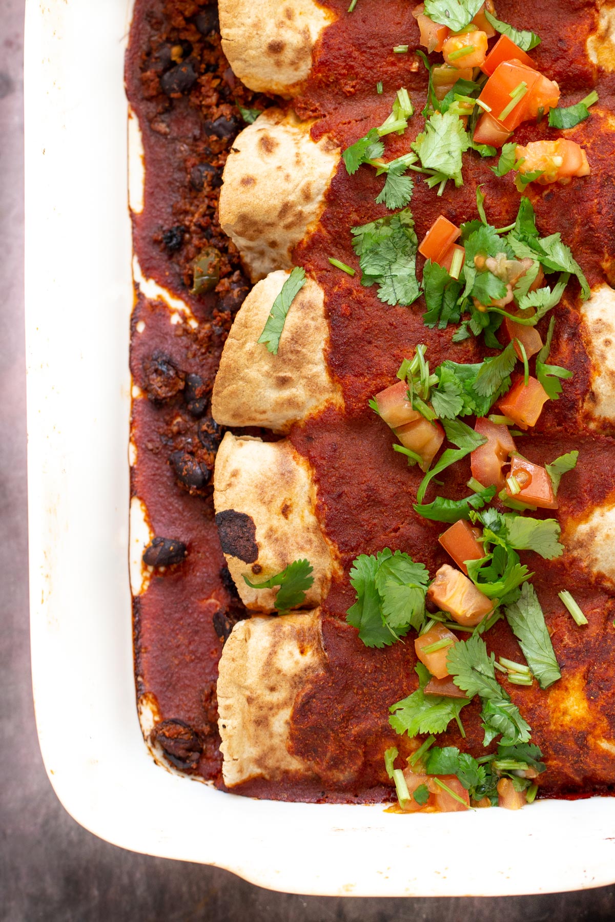 a casserole dish with vegan enchiladas covered with tomato sauce and topped with cilantro