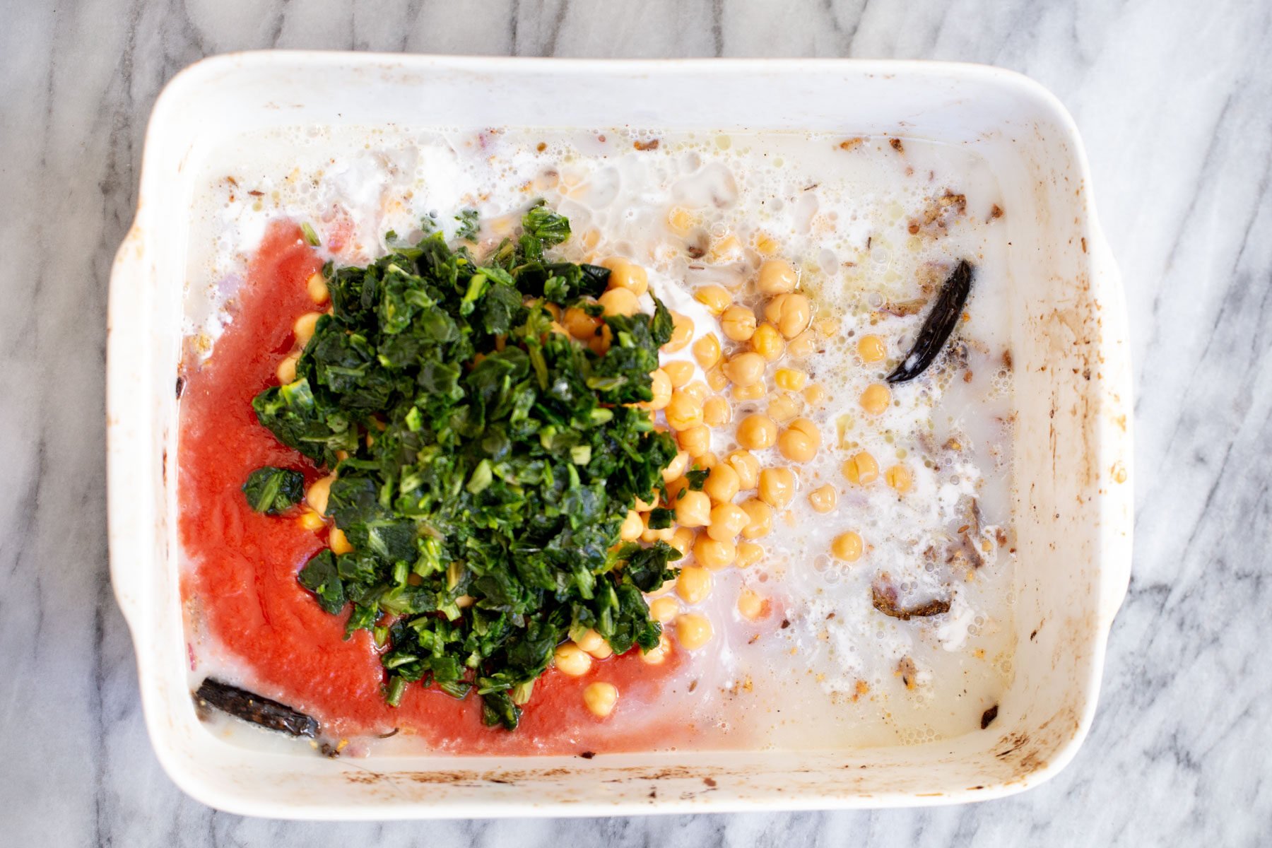 spinach and chickpeas being added to a casserole dish