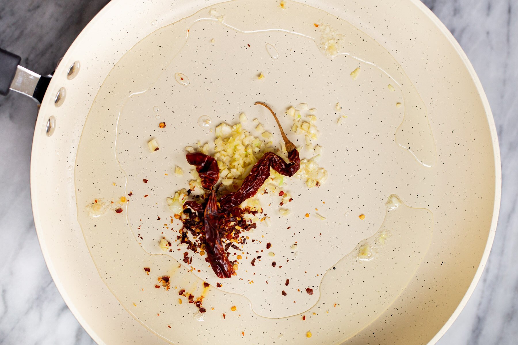 chili and garlic frying in oil in a white pan
