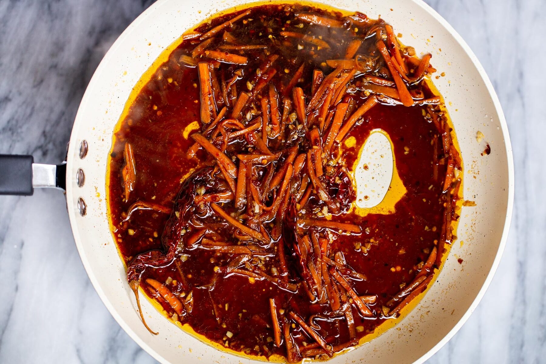 stir-fry sauce being added to sauteed carrots in a white pan
