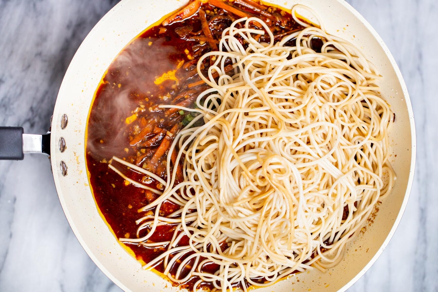 cooked noodles being added to stir-fry sauce in a white pan