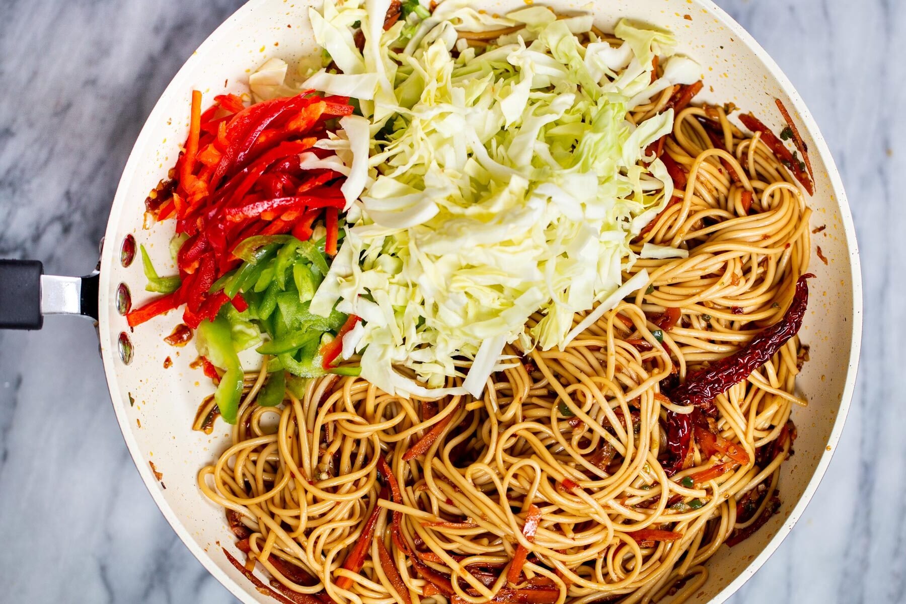 bell pepper and chopped cabbage being added to sauteeing pan with noodles
